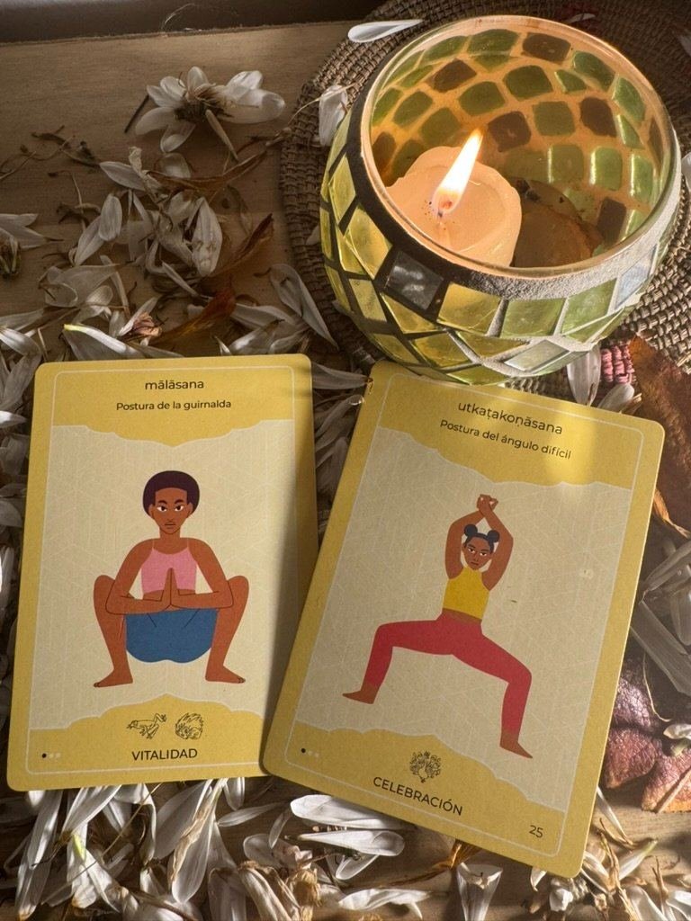 Dos cartas ICCHĀ —mālāsana y uṭkaṭakoṇāsana— junto a una vela encendida